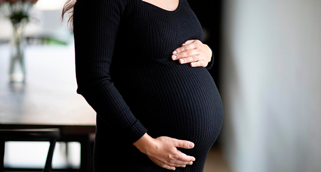 Gravid kvinde står med hænderne om livet